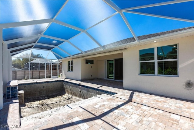 exterior space with stucco siding, a shingled roof, a patio area, glass enclosure, and fence