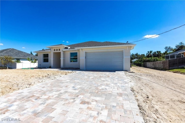 prairie-style house with decorative driveway, fence, an attached garage, and stucco siding