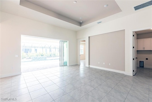 spare room featuring a tray ceiling, visible vents, baseboards, and light tile patterned flooring