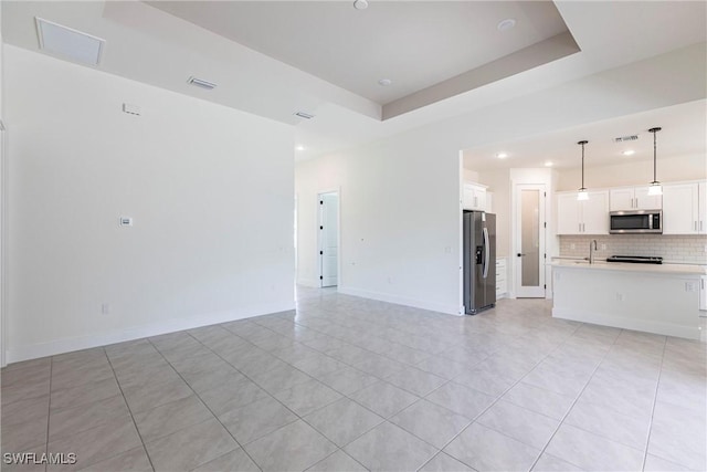 unfurnished living room with light tile patterned floors, a sink, visible vents, baseboards, and a tray ceiling