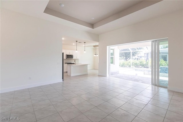 unfurnished living room with a tray ceiling, baseboards, and light tile patterned floors