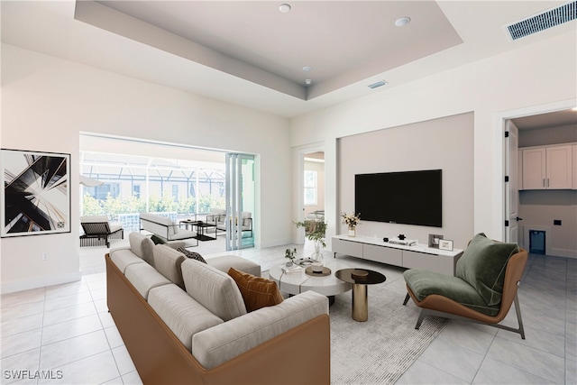 living room with a tray ceiling, visible vents, baseboards, and light tile patterned floors