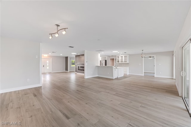 unfurnished living room featuring a chandelier, light wood finished floors, a fireplace, and baseboards