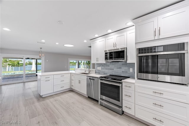 kitchen featuring a peninsula, white cabinets, light countertops, appliances with stainless steel finishes, and decorative backsplash