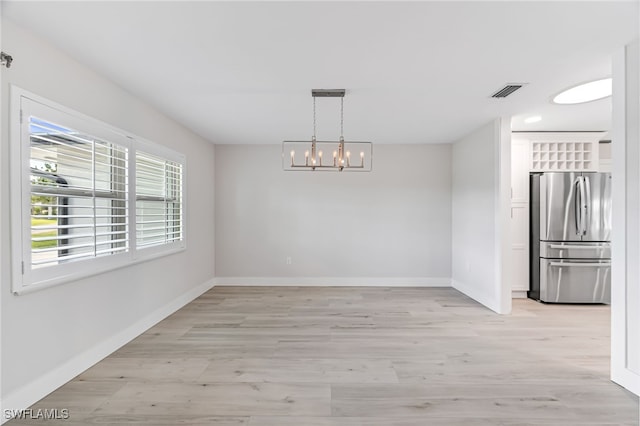 unfurnished dining area featuring an inviting chandelier, light wood-type flooring, visible vents, and baseboards