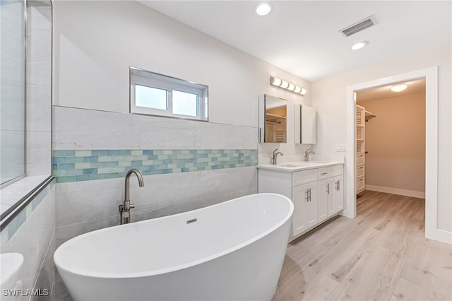 bathroom with tile walls, double vanity, visible vents, a sink, and a freestanding tub