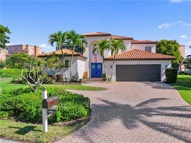 mediterranean / spanish house featuring decorative driveway, a tile roof, an attached garage, and stucco siding