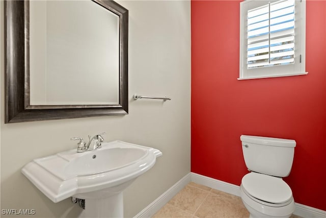 half bathroom featuring baseboards, a sink, toilet, and tile patterned floors