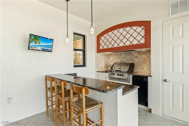 kitchen featuring visible vents, a kitchen breakfast bar, black dishwasher, backsplash, and dark stone countertops