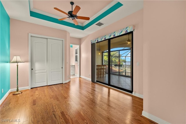 unfurnished bedroom with a raised ceiling, visible vents, wood finished floors, access to outside, and baseboards