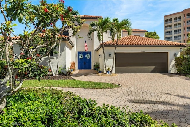 mediterranean / spanish-style house with decorative driveway, an attached garage, a tile roof, and stucco siding