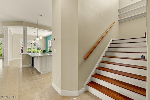 stairs with baseboards, a chandelier, tile patterned flooring, and ornate columns