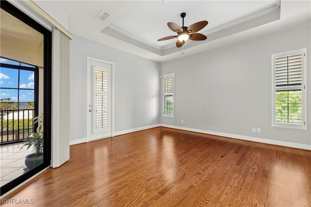 spare room featuring crown molding, a raised ceiling, plenty of natural light, and wood finished floors