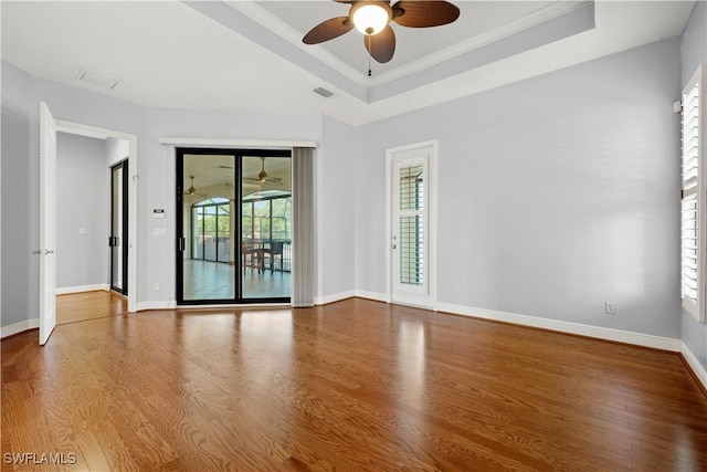 spare room with a raised ceiling, visible vents, ceiling fan, wood finished floors, and baseboards