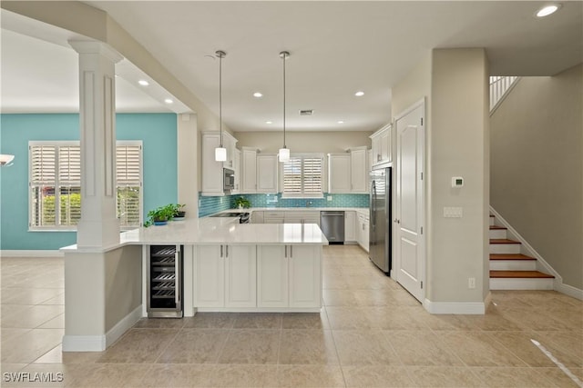 kitchen featuring wine cooler, a peninsula, light countertops, appliances with stainless steel finishes, and tasteful backsplash