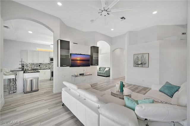 living area with arched walkways, light wood-style flooring, visible vents, and recessed lighting