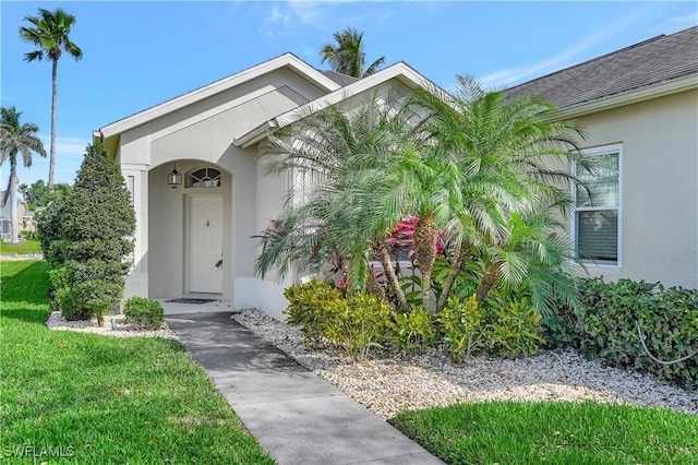 property entrance with a shingled roof, a lawn, and stucco siding