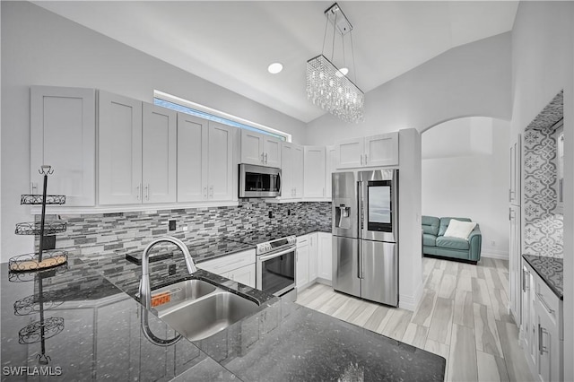 kitchen featuring arched walkways, stainless steel appliances, a sink, hanging light fixtures, and dark stone counters