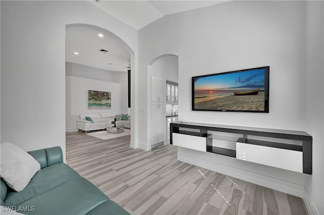 living area with arched walkways, recessed lighting, baseboards, vaulted ceiling, and light wood-style floors