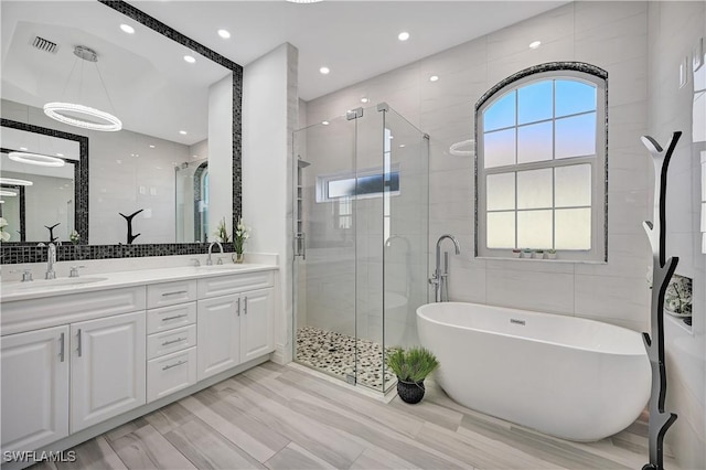 full bath featuring a freestanding tub, visible vents, tile walls, and a sink