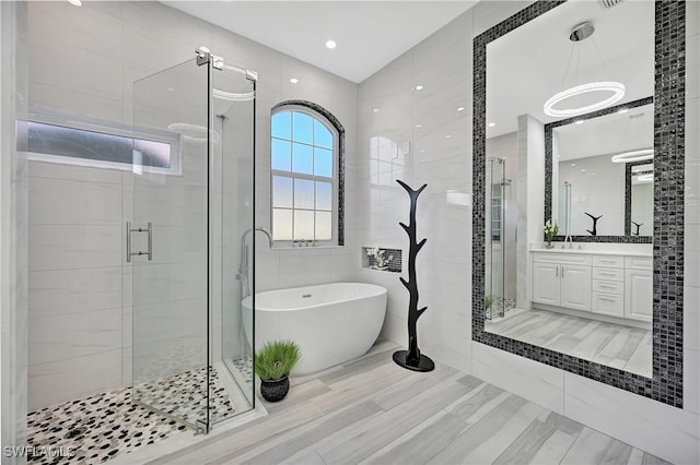 bathroom featuring tile walls, a freestanding tub, a shower stall, and vanity