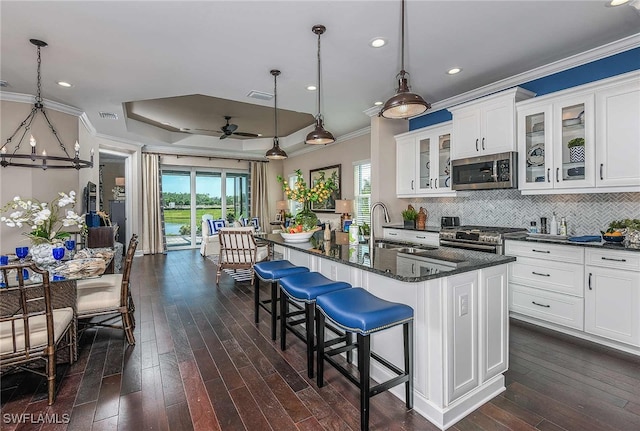 kitchen with a kitchen island with sink, white cabinetry, hanging light fixtures, appliances with stainless steel finishes, and glass insert cabinets