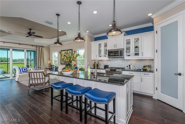 kitchen featuring a sink, white cabinets, hanging light fixtures, appliances with stainless steel finishes, and glass insert cabinets