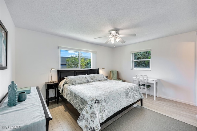 bedroom with light wood finished floors, a textured ceiling, baseboards, and a ceiling fan