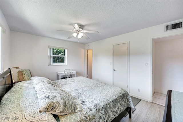 bedroom with light wood finished floors, visible vents, a ceiling fan, a textured ceiling, and baseboards