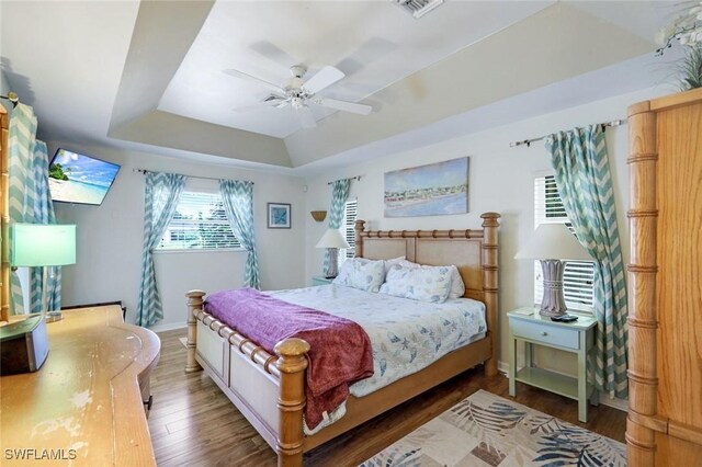 bedroom with a raised ceiling, visible vents, ceiling fan, wood finished floors, and baseboards