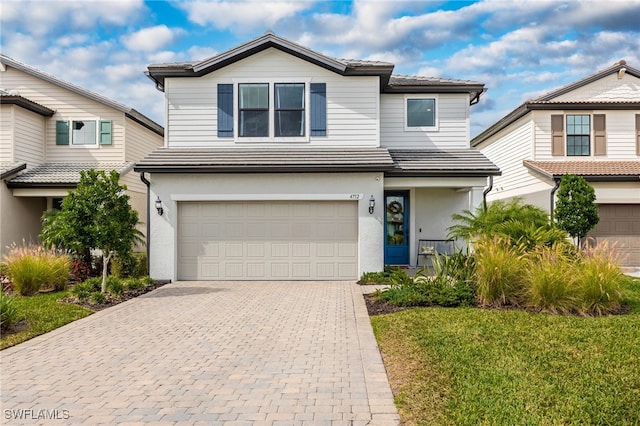 traditional-style house featuring decorative driveway, stucco siding, an attached garage, and a tile roof