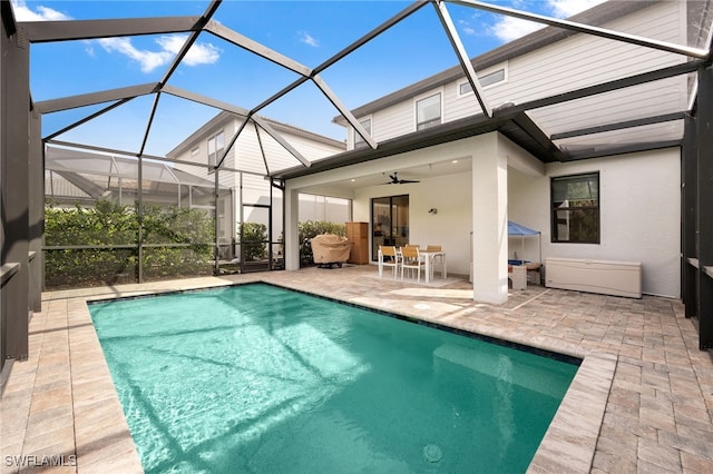 outdoor pool with glass enclosure, a patio area, and a ceiling fan