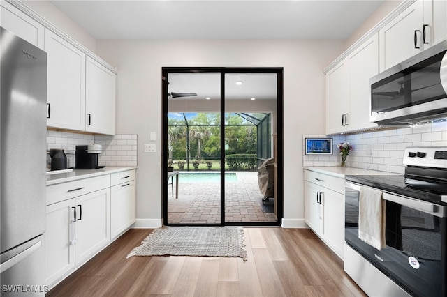 kitchen featuring light wood finished floors, a sunroom, light countertops, white cabinets, and appliances with stainless steel finishes