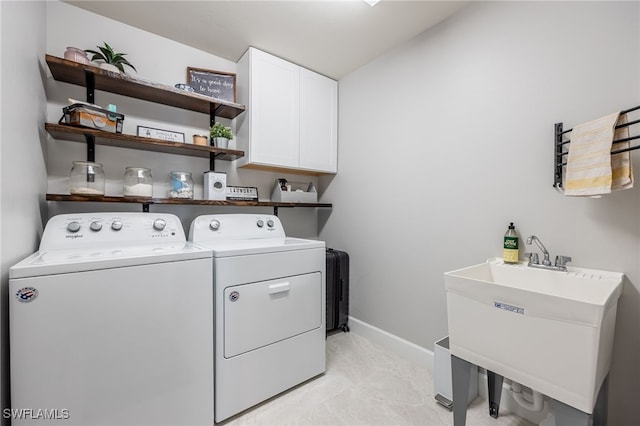 clothes washing area featuring a sink, baseboards, cabinet space, and separate washer and dryer