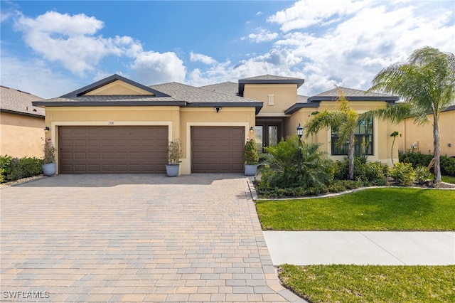 prairie-style house with stucco siding, a front yard, decorative driveway, and a garage