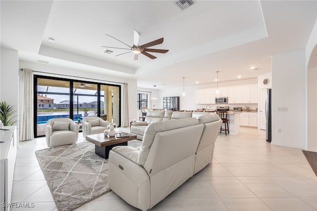 living area with visible vents, a tray ceiling, recessed lighting, light tile patterned flooring, and ceiling fan