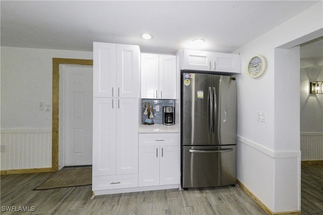 kitchen featuring light countertops, light wood-style flooring, freestanding refrigerator, wainscoting, and white cabinetry