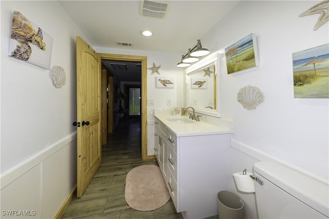 half bathroom featuring toilet, vanity, visible vents, and wainscoting