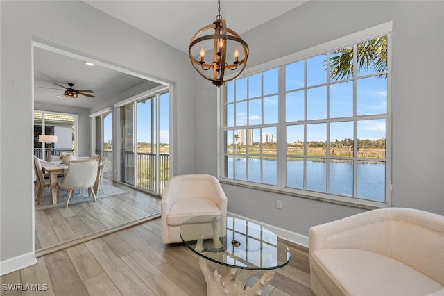 living area featuring ceiling fan with notable chandelier, a water view, wood finished floors, and baseboards