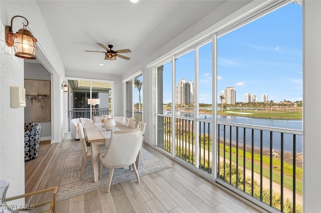 sunroom with ceiling fan, a water view, and a city view