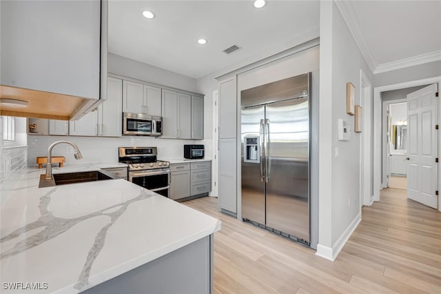 kitchen featuring tasteful backsplash, appliances with stainless steel finishes, light stone counters, gray cabinetry, and a sink