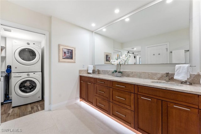 clothes washing area with light tile patterned floors, baseboards, stacked washing maching and dryer, a sink, and recessed lighting