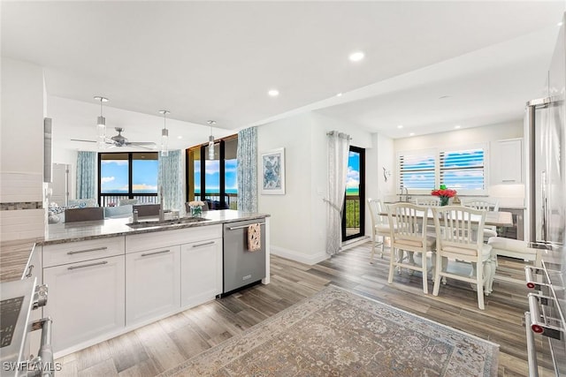 kitchen with light stone counters, stainless steel appliances, a peninsula, a sink, and white cabinets