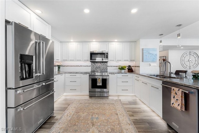 kitchen featuring white cabinets, appliances with stainless steel finishes, dark stone countertops, light wood-style floors, and a sink