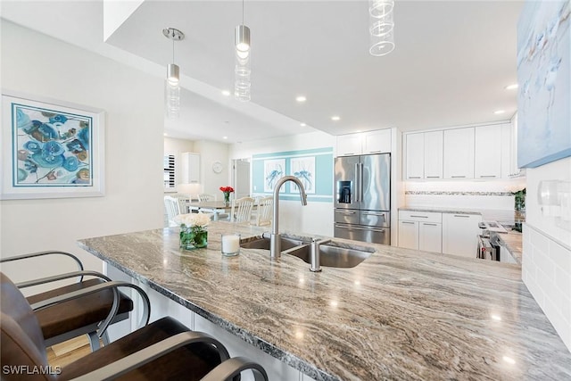 kitchen featuring tasteful backsplash, high quality fridge, a sink, light stone countertops, and a peninsula