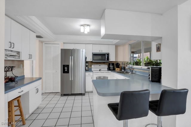 kitchen with light tile patterned floors, white cabinets, a peninsula, stainless steel appliances, and a kitchen bar