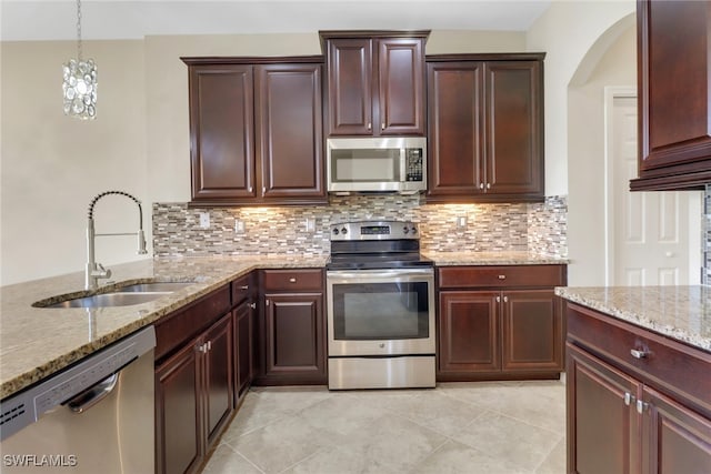 kitchen featuring decorative backsplash, a sink, stainless steel appliances, arched walkways, and light stone countertops