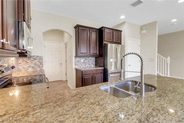 kitchen with light stone countertops, a sink, visible vents, arched walkways, and appliances with stainless steel finishes