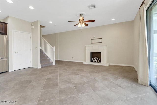 unfurnished living room with light tile patterned floors, a ceiling fan, visible vents, and stairs