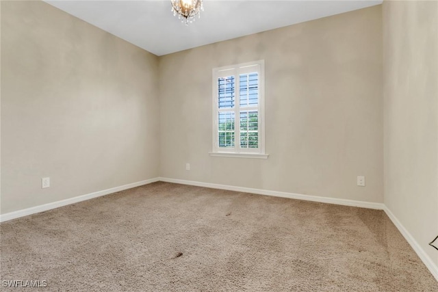 carpeted spare room with a chandelier and baseboards